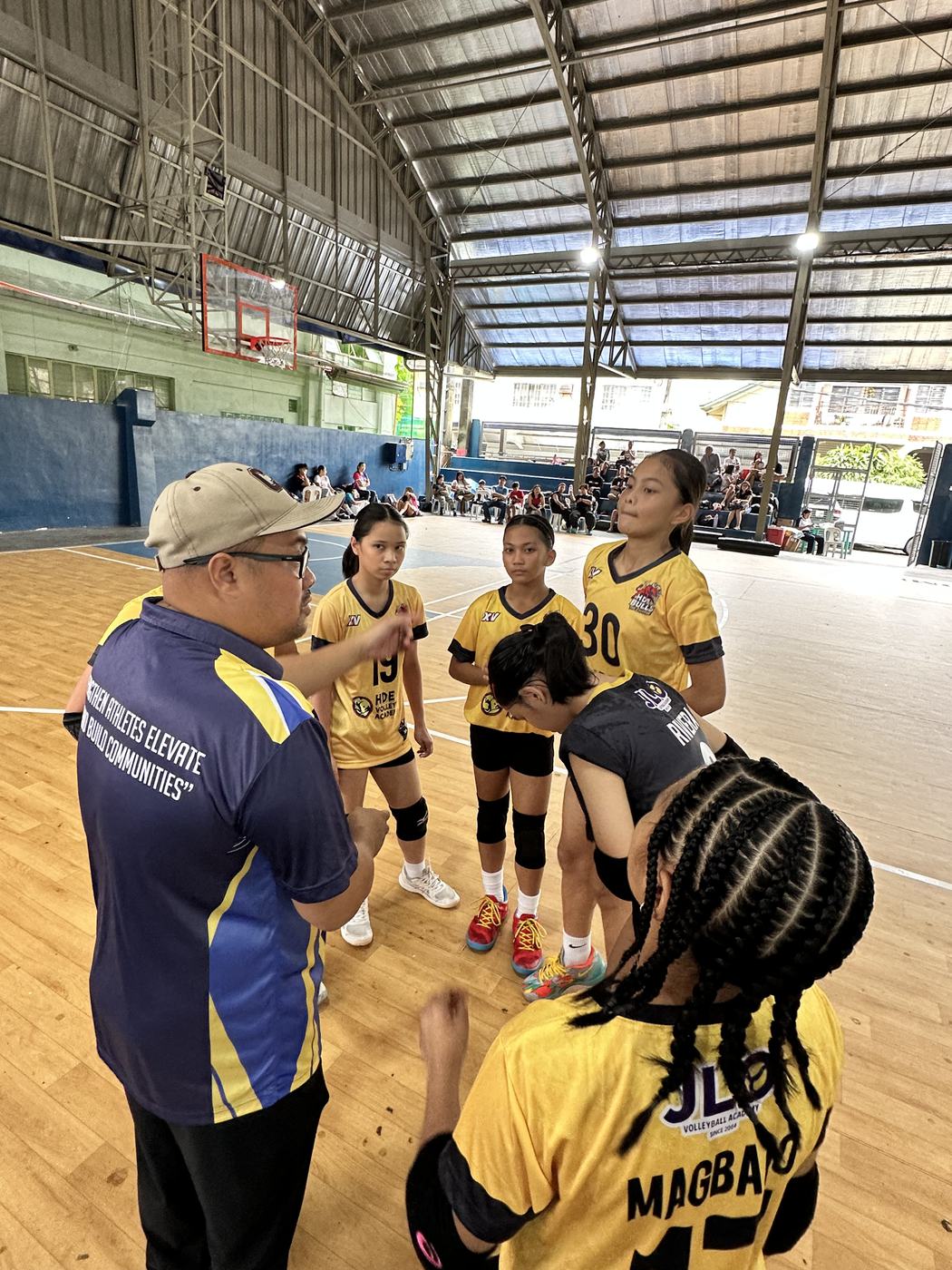 An HDE coach talks with players in gold and black during a game