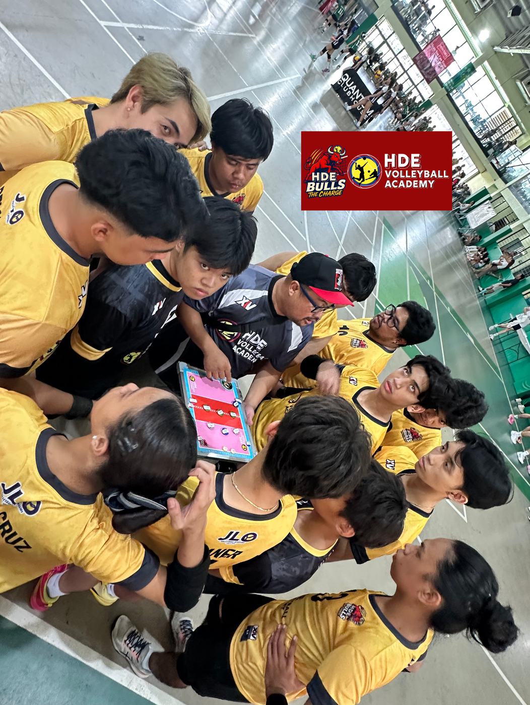 HDE players in gold huddle around a clipboard under the HDE Bulls banner