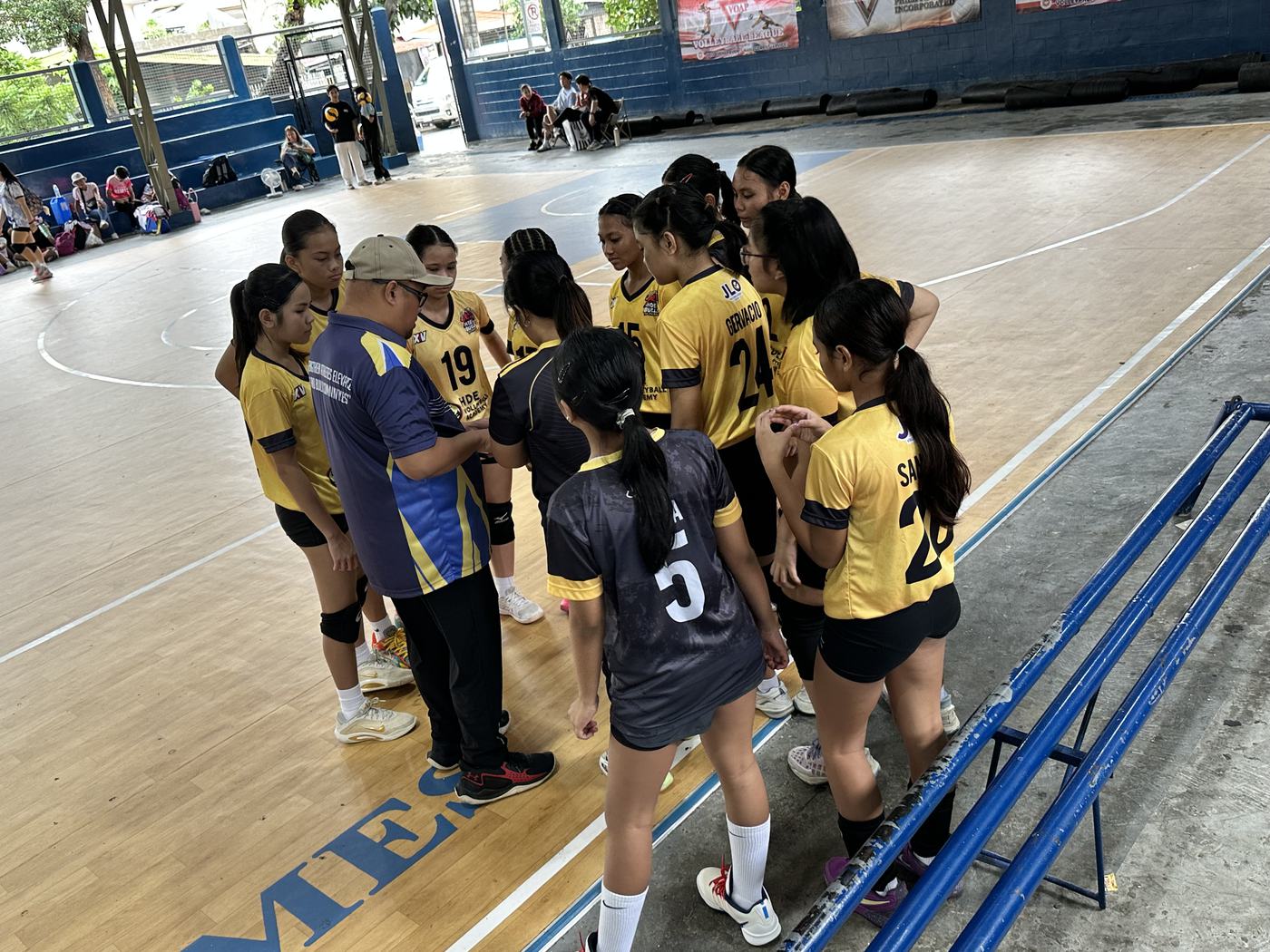 An HDE coach gathers his team in gold and black on a wooden court