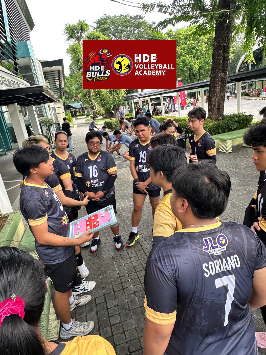 Players in JLO jerseys gather around a coach outdoors under the HDE Bulls banner