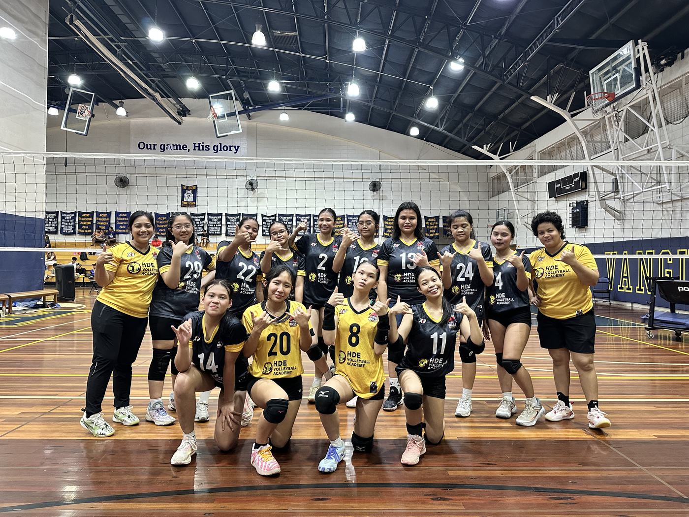 An HDE team in gold and black posing with coaches in a gym