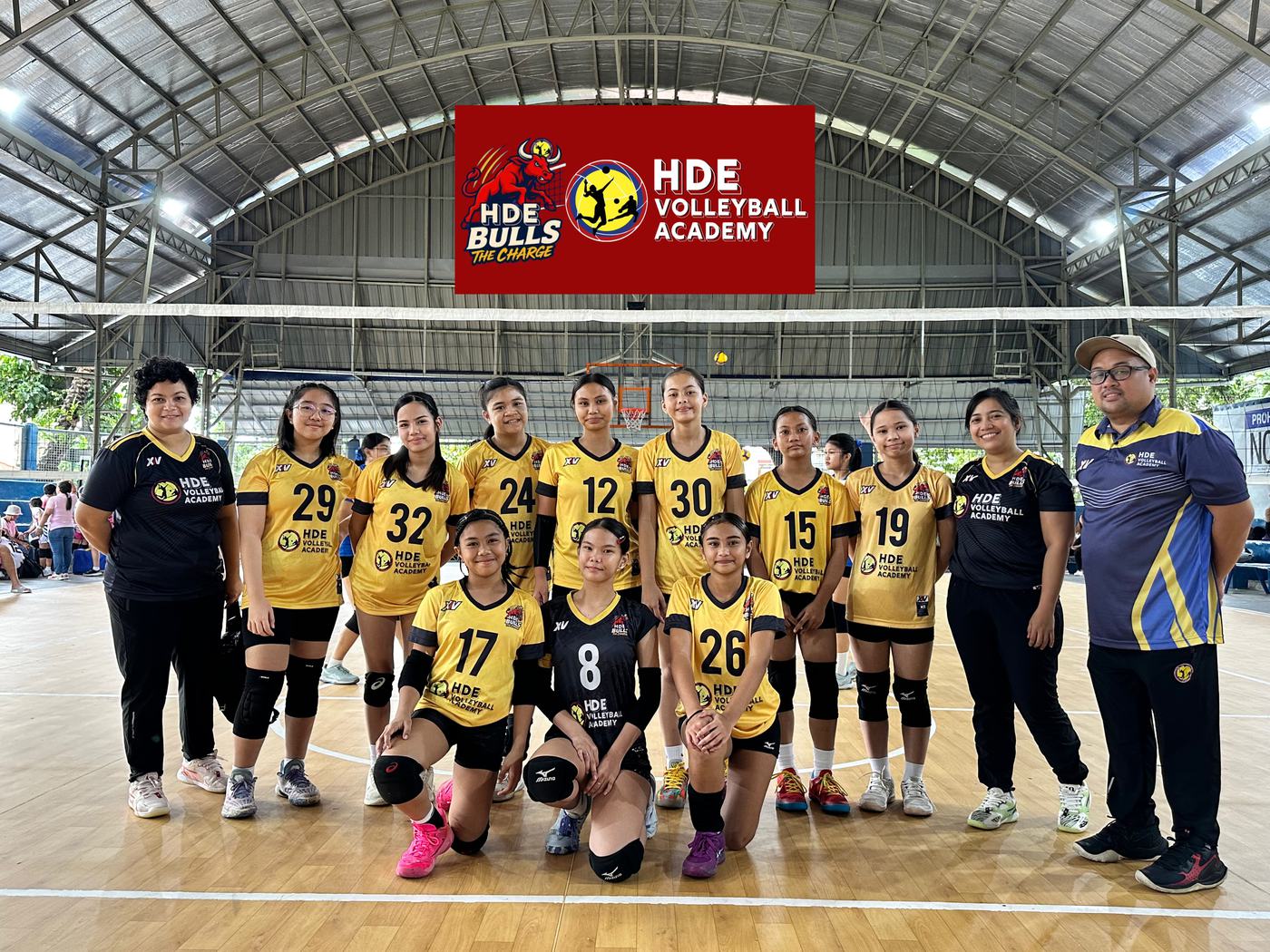 HDE Bulls players in gold and black with their coaches under the HDE Bulls banner