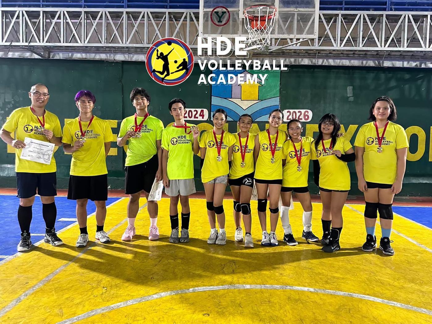 Medal winners in yellow and green jerseys at an awarding under the HDE Volleyball Academy banner