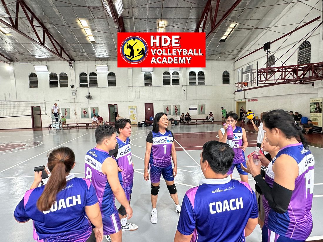 Two HDE coaches talking with their players in a team huddle under the HDE Volleyball Academy banner